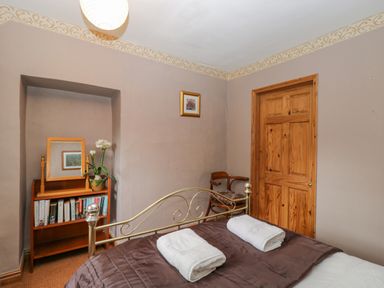 A bedroom with a bed with towels on it a wooden door a small bookshelf with books and a mirror and a chair at Field Cottage in Shepton Mallet