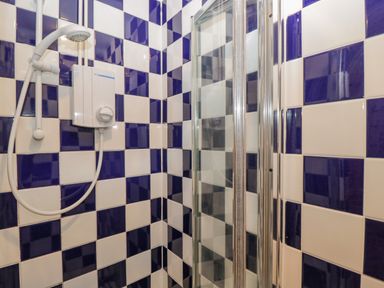 A shower area with blue and white checkered tiles and a white showerhead and control unit at Field Cottage in Shepton Mallet