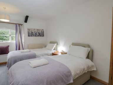 A bedroom with two single beds white bedding purple blankets and a window with purple and white curtains at Field Cottage in Shepton Mallet