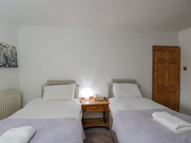 A bedroom with two single beds separated by a wooden nightstand with a lamp at Field Cottage in Shepton Mallet