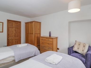 A bedroom with two single beds wooden wardrobe wooden chest of drawers and a purple armchair at Field Cottage in Shepton Mallet