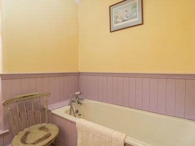 A bathroom with a bathtub a towel hanging on the tub and a wooden chair next to it at Field Cottage in Shepton Mallet