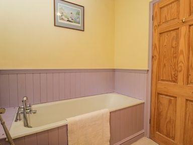 A bathroom with a bathtub with a towel hanging over the side and a wooden door at Field Cottage in Shepton Mallet
