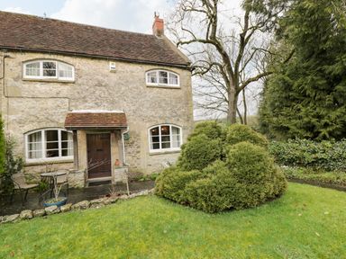 A stone cottage with a small patio and table with chairs and trimmed bushes in the garden at Field Cottage in Shepton Mallet