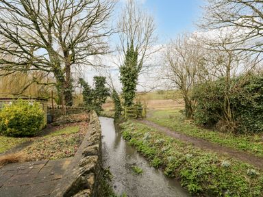 A small stream with a stone wall and trees surrounding it at Field Cottage in Shepton Mallet
