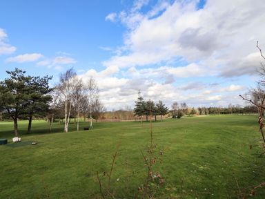 A grassy field with scattered trees under a partly cloudy sky at Lodge 1 in South Hykeham