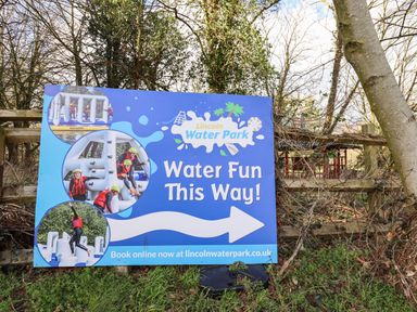 A sign for Lincoln Water Park with images of people in helmets and life jackets on inflatable water structures at Lodge 1 South Hykeham