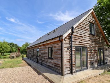 A wooden exterior of a house with multiple windows and doors next to a gravel area and trees at Lodge 24 in South Hykeham