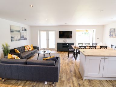 An open living room and dining area with gray sofas a round black coffee table a wooden dining table with black chairs and a TV mounted on the wall at Lodge 24 in South Hykeham