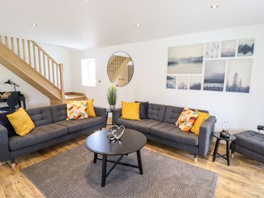 A living room with two gray sofas and yellow cushions a round black coffee table wooden stairs and wall art at Lodge 24 in South Hykeham