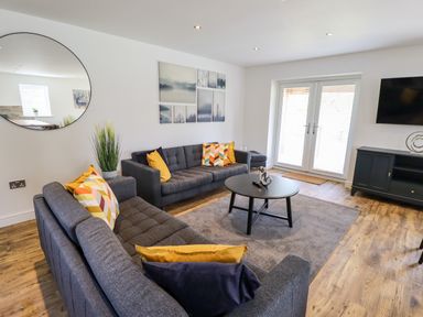 A living room with two grey sofas yellow and patterned cushions a round black coffee table a large round mirror and a TV cabinet at Lodge 24 in South Hykeham