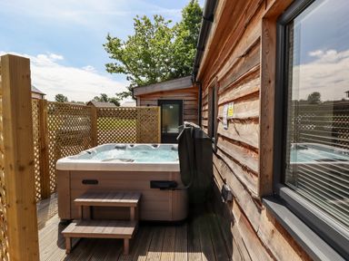 An outdoor hot tub with steps next to a wooden building and lattice fencing at Lodge 24 in South Hykeham