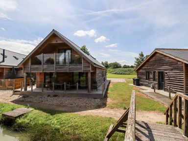 Two wooden buildings with outdoor seating and a small wooden bridge near a pond at Lodge 24 in South Hykeham