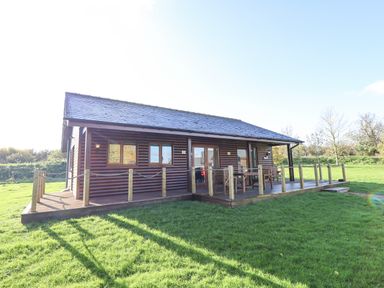 A wooden cabin with deck and outdoor seating on grass at Lodge 2 in South Hykeham