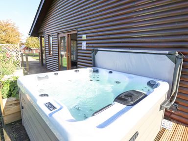 An outdoor hot tub filled with water next to a wooden cabin with sliding glass doors at Lodge 2 in South Hykeham