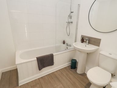 A bathroom with a bathtub shower combination a white sink a toilet a round mirror and a gray towel at Lodge 2 in South Hykeham