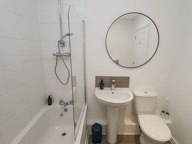 A bathroom with a bathtub shower, a sink with a mirror above it, and a toilet at Lodge 2 in South Hykeham