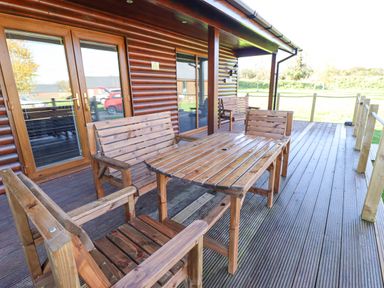 An outdoor wooden deck with chairs and tables outside a wooden cabin at Lodge 2 in South Hykeham
