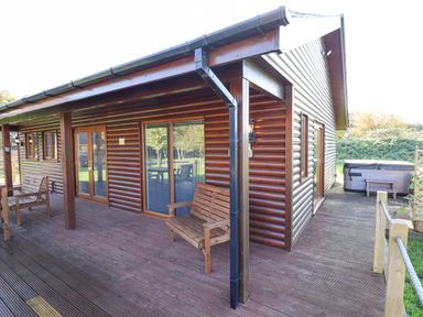 Exterior view of a wooden lodge with outdoor benches on a deck and a hot tub at Lodge 2 in South Hykeham