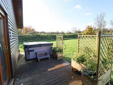 A wooden deck with a hot tub and lattice planters next to a grassy yard at Lodge 2 in South Hykeham