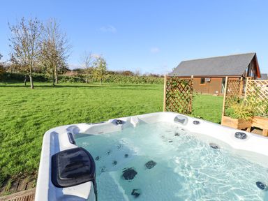 An outdoor hot tub with water in a grassy area near a wooden cabin and lattice panels at Lodge 2 in South Hykeham