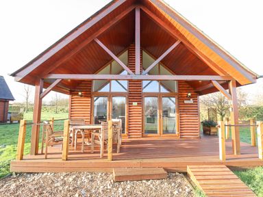 A wooden cabin with a porch and outdoor furniture in a grassy area at Lodge 4 in South Hykeham