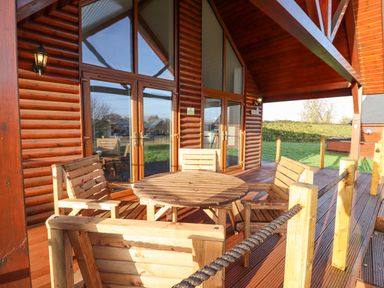 A wooden outdoor deck with a round table and four chairs outside a log cabin at Lodge 4 in South Hykeham