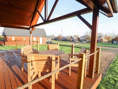 A wooden patio with a table and chairs under a wooden roof at Lodge 4 in South Hykeham