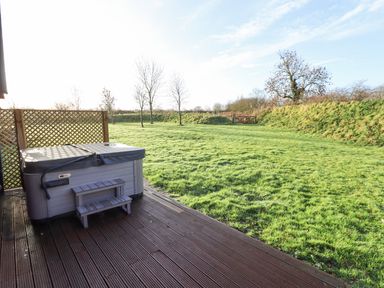 An outdoor deck with a covered hot tub and steps overlooking a grassy yard with trees and a wooden gate at Lodge 4 in South Hykeham