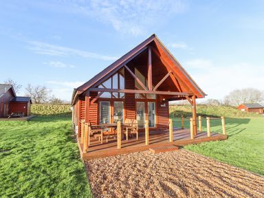 A wooden cabin with a deck and outdoor furniture on grass at Lodge 7 in South Hykeham