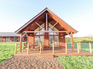A wooden cabin with a patio and outdoor furniture surrounded by grass at Lodge 7 in South Hykeham