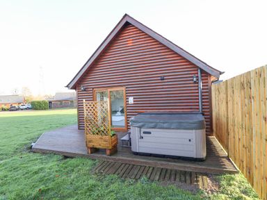 An outdoor wooden deck with a hot tub next to a log cabin at Lodge 7 in South Hykeham