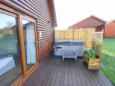 An outdoor wooden deck with a hot tub small steps and planter next to a wooden house at Lodge 7 in South Hykeham