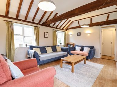 A living room with blue and red sofas a wooden coffee table and exposed wooden ceiling beams at The Brambles in Polstead