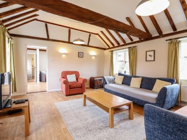 A living room with a blue sofa, red armchair, wooden coffee table, television, and exposed ceiling beams at The Brambles in Polstead