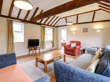 A living room with wooden beams on the ceiling a wooden table a television and seating at The Brambles in Polstead