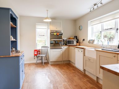 A kitchen with cream cabinets a blue cupboard wooden countertops and a chair by the window at The Brambles in Polstead