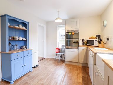 A kitchen with a blue cupboard and white cabinets with appliances and a chair in the corner at The Brambles in Polstead
