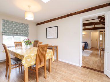 A dining room with a wooden table and chairs a yellow tablecloth and flowers in a vase at The Brambles in Polstead