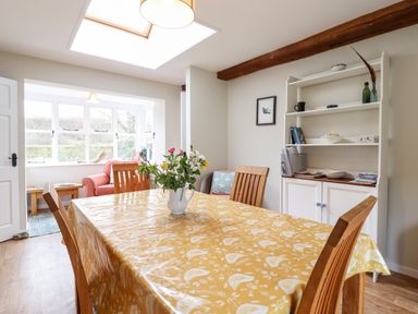 A dining room with wooden table and chairs a white cabinet and a seating area with windows at The Brambles in Polstead