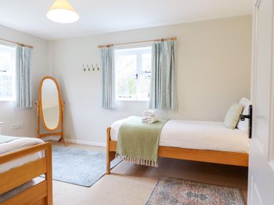 A bedroom with two single beds a standing mirror and two windows with curtains at The Brambles in Polstead
