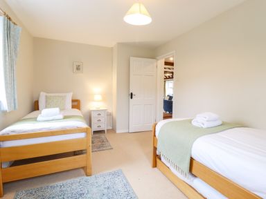 A bedroom with two single beds a bedside table and lamp and an open door at The Brambles in Polstead