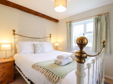 A bedroom with a metal bed frame a nightstand with lamp and a window with curtains at The Brambles in Polstead
