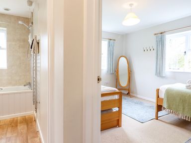 A bathroom with a bathtub and a bedroom with two single beds a mirror and windows at The Brambles in Polstead
