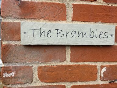 A sign reading The Brambles on a red brick wall at The Brambles in Polstead