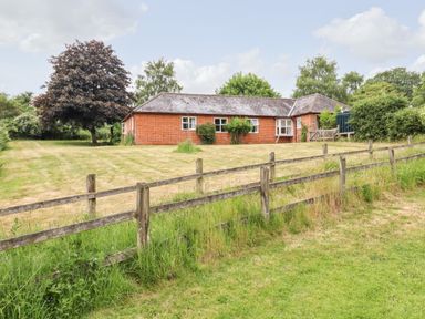 A single-story brick house with a slate roof surrounded by a grassy yard and wooden fence at The Brambles in Polstead