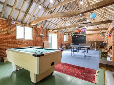 A game room with a pool table and ping pong table with decorations hanging from the ceiling at The Brambles in Polstead