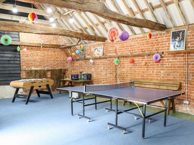 A game room with a table tennis table foosball table and wooden bench under exposed beams at The Brambles in Polstead