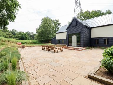 A patio with wooden bench seating outside a black and cream building with a metal roof at The Brambles in Polstead