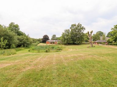A grassy field with trees and a red brick building in the distance at The Brambles in Polstead